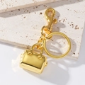 Goldener Handtaschen-Schlüsselanhänger mit Federhaken auf beigem Travertin-Hintergrund - Gold
