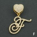 Macro shot of gold-plated iced-out letter F pendant with heart clasp on black texture - Letter F / Gold