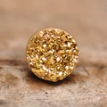 Dettaglio macro di un orecchino magnetico dorato rotondo con superficie in cristallo testurizzato - Druzy Oro