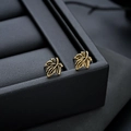 Macro shot of vintage golden maple leaf studs with textured veins on leather - Antique Gold