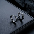 Detalle de pendientes huggie color gunmetal con grabado sobre expositor de cuero negro - Color gunmetal
