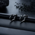 Macro shot of dark gunmetal Mobius screw clip-on earrings on black leather texture - Black