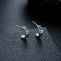 Detailansicht der silbernen C-förmigen Ohrstecker mit grünen geometrischen Emaille-Mustern - Grün