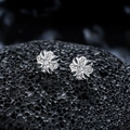 Macro shot of silver iris cross stud earrings with sparkling zircons on black stone - Silver Cross Flower