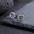 Macro shot of titanium steel H-letter stud earrings on a dark volcanic rock background - Silver