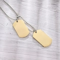 Vue macro de pendentifs militaires dorés mats avec chaîne à billes sur bois blanc - Or