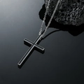 Minimalist black cross pendant with silver metal chain on dark volcanic stone background - Silver