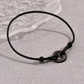Minimalist black cord bracelet with adjustable metal ring on a grey textured background - Black