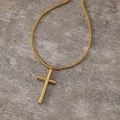 Detailed close-up of a polished gold cross pendant with a tubular design on a box chain - Gold