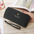 Detail of black pebbled leather wallet with golden deer ornament and hand strap on wood - Black