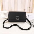 Black quilted crossbody cell phone bag with gold floral buckle on a wooden background - Black