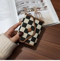 Classic black and white checkered wallet with brown leather trim held over a desk - Coffee Plaid