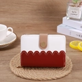 Detail view of wave-edged short wallet with gold zipper on a cozy coffee table setting - Burgundy