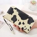 Women's long cow print zipper wallet with wrist strap held by hand in home setting - Light Yellow