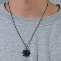 Dettaglio del ciondolo a sole con pietra nera su collana indossata su maglia grigia - Nero sole