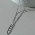 Collar minimalista de plata con colgante geométrico pulido sobre fondo gris moderno - Color Acero