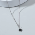 Minimalist silver chain necklace with a black round pendant on a smooth grey surface - Round