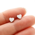 Dettaglio di piccoli orecchini a cuore in acciaio inossidabile argento tenuti in mano - Color Acciaio