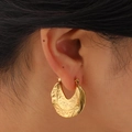 Detailed close-up of golden irregular textured C-shaped hoop earrings on female model - Gold