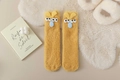Detailansicht gelber Plüschsocken mit lustigen 3D-Augen auf weißem Kunstfell-Teppich - Gelber Monsterstil / Hellgelb