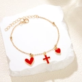 Pulsera dorada con dijes de corazón rosa y cruz mostrada sobre una elegante piedra blanca - Rojo