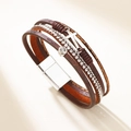 Bracelet multicouche en cuir avec breloque croix et fermoir magnétique sur fond beige uni - Marron