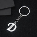 Silver metal letter D keychain with sparkling rhinestones on a textured black background - Letter D