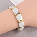 Dettaglio di bracciale in ceramica bianca con maglie dorate a forma di H al polso - Oro Bianco