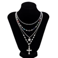 Detail of layered silver necklace featuring a sun charm, pearl strand, and colorful crystal cross - Silver