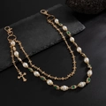 Detail of gold pants chain featuring pearls, green gems, and a colorful cross pendant - Gold