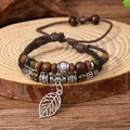 Close-up of woven leather bracelet with wood beads and hollow leaf metal charm - Bracelet 17