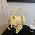 Cremegelbe Boston Bag mit Griffen, Knotendetails und einem Herzspiegel-Anhänger - Gelb