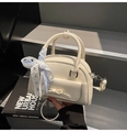 Crèmewitte mini Boston tas met blauw geruit lint en strikdetail geplaatst op zwarte boeken - Wit