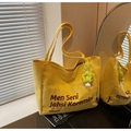 Detail shot of yellow canvas tote bag featuring brown typography and a green plush flower charm - Yellow with Pendant
