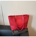 Dettaglio della borsa tote in pelle martellata rossa con manici sottili su un libro - Rosso
