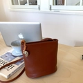 Sac seau minimaliste en cuir marron pour femme avec charme argenté sur fond bois - Marron avec pendentif