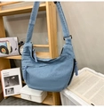 Close-up of light blue denim crescent crossbody bag on a shelf with woven zipper pull - Light Blue