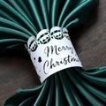 White laser-cut Merry Christmas napkin ring featuring three Santa Claus heads on green fabric - White