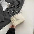 Sac bandoulière crème avec chaîne et breloque camélia posé sur un blazer gris - Blanc Petit