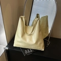 Minimalist pale yellow leather tote bag with wide shoulder strap on a sleek black desk - Yellow