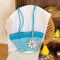 Handmade woven blue and beige straw tote bag with sunflower pendant on a wooden chair - Blue with Charm