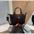 Close-up of black nylon crossbody bag featuring round metal logo and wide fabric shoulder strap - Black