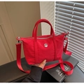 Detailed shot of a red canvas crossbody bag with silver logo and woven shoulder strap - Burgundy