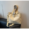 Détail du sac cabas en toile beige avec bandoulière et logo posé sur un livre - Blanc Cassé