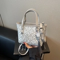 Sac seau beige gris avec broderie florale et pompon décoratif posé sur un livre d'art - Gris