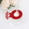 Vue macro d'un marque-place rouge pailleté en forme de bague diamant sur un verre à pied - Rouge Pailleté