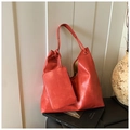 Détail du sac hobo en cuir orange avec petite pochette assortie posé sur un livre - Rouge