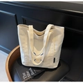 Close-up of cream canvas tote bag with blue stitching detail on a black leather chair - Off-white