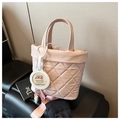 Close-up of pink quilted bucket bag with Capybara charm and branding on black bench - With Charm / Pink