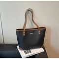 Detail of black pebbled leather tote bag with brown trim and gold hardware accents - Black
